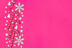 weihnachtszuckerstange lag gleichmäßig in reihe auf rosa hintergrund mit dekorativer schneeflocke und stern. flache Lage und Draufsicht foto