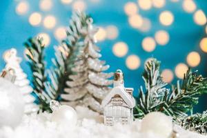 abstrakter Adventsweihnachtshintergrund. Spielzeugmodellhaus und Winterdekorationsverzierungen auf blauem Hintergrund mit Schnee. weihnachten mit familienkonzept zu hause. foto