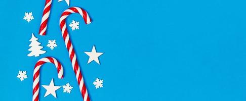 Weihnachtszuckerstange lag gleichmäßig in Reihe auf blauem Hintergrund mit dekorativer Schneeflocke und Stern. flache Lage und Draufsicht foto
