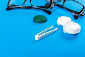 Kontaktlinsen mit Kunststoffgehäuse und Pinzette mit Brille auf dem Hintergrundplan auf lila Hintergrund. wie Kontaktlinsen aufzubewahren und zu verwenden sind foto