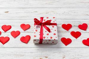 valentinstag oder andere handgemachte feiertagsgeschenke in papier mit roten herzen und geschenkbox in feiertagsverpackung. Präsentkarton mit Geschenk auf weißer Holztischplatte mit Kopierraum, leerer Raum für Design foto