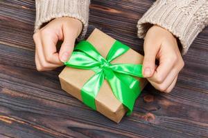 Mädchen, das eine einfache grüne Schleife auf einer Geschenkbox bindet. Eingewickelt in einfaches Bastelpapier und blaues Band. Feinschliff foto