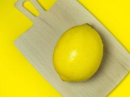 eine ganze Zitrone auf einem Schneidebrett auf gelbem Hintergrund. Zitrusfrüchte auf dem Tisch. heller Hintergrund. Gesundes angereichertes Lebensmittel für eine Diät. foto