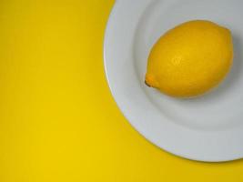 eine ganze Zitrone auf einem Teller auf weißem Hintergrund. Zitrusfrüchte auf dem Tisch. Gesundes angereichertes Lebensmittel für Vegetarier.Zitronenisolat foto