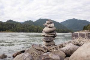 eine Pyramide aus nackten Steinen, die übereinander gestapelt sind. Steine, die in Form einer Pyramide am Flussufer vor dem Hintergrund der Berge gestapelt sind, als Gleichgewicht und Gleichgewicht in der Natur, Zen, Buddhismus. foto