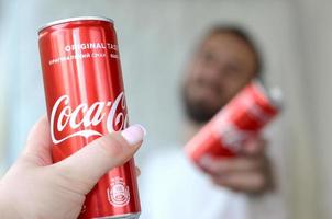 Charkow. ukraine - 2. mai 2022 glücklicher junger mann hebt coca-cola-blechdose mit freundin im garageninnenraum auf foto