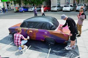 charkow, ukraine - 27. mai 2022 festival der straßenkunst. junge kerle malen graffiti auf die autokarosserie im stadtzentrum. der Prozess, Farbgraffiti mit Aerosoldosen auf ein Auto zu malen foto