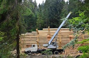 der Prozess des Baus eines Holzhauses aus Holzbalken mit zylindrischer Form. Kran in funktionstüchtigem Zustand foto