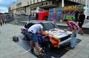 charkow, ukraine - 27. mai 2022 festival der straßenkunst. junge kerle malen graffiti auf die autokarosserie im stadtzentrum. der Prozess, Farbgraffiti mit Aerosoldosen auf ein Auto zu malen foto