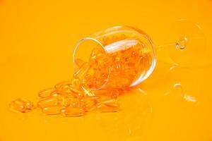 Fischölkapseln. Gelbe Omega-3-Pillen im Glas auf Gelb und Orange. Fischölkapseln im Glas. im Glas. in Eimerampullen foto
