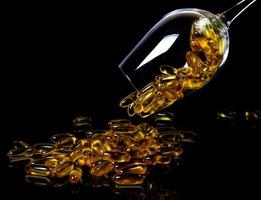 Fischölkapseln. gelbe omega-3-pillen im glas auf dem dunklen schwarz. Fischölkapseln im Weinglasglas. im Glas. in Eimerampullen foto