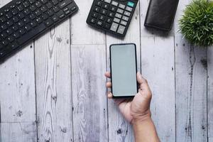 flache zusammensetzung der hand, die smartphone auf schreibtisch hält foto