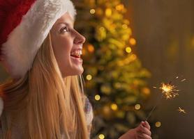 Porträt des lächelnden Teenager-Mädchens in der Weihnachtsmütze, die Wunderkerzen hält foto