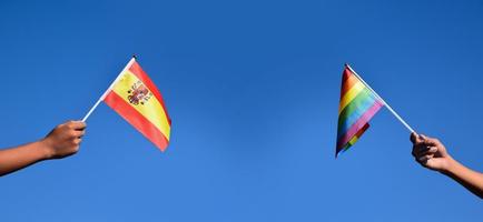 spanische flagge und regenbogenfahne, die in händen und gegen bluesky, weicher und selektiver fokus, konzept für lgbt-feiern und lgbt-veranstaltungen im stolzmonat in spanien gehisst werden. foto