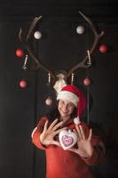 Frau. Claus steht unter geschmücktem Geweih und hält herzförmige Weihnachtskugel foto