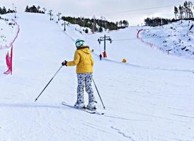Rückansicht der jungen Frau in gelber Jacke und Skihelm beim Skifahren am Berghang, Wintersport, alpines Skifahren im Freien, gesunder Lebensstil foto