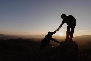 Silhouetten von zwei Menschen, die auf den Berg klettern und helfen. hilfe- und assistenzkonzept. foto