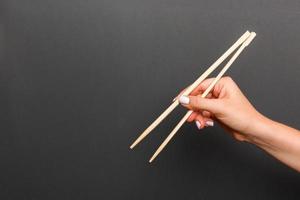 kreatives Bild von Holzstäbchen in weiblicher Hand auf schwarzem Hintergrund. japanisches und chinesisches essen mit kopierraum foto