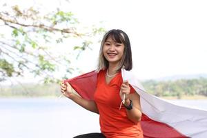 schöne junge asiatin, die die indonesische flagge mit einem fröhlichen gesicht trägt foto