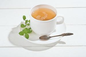 Kräutertee mit Minze auf einem weißen Holztisch. Alternativmedizin für die Gesundheit des Magen-Darm-Systems und Linderung von Angstzuständen. beruhigendes und wohltuendes Abendgetränk foto