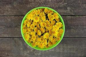 Grüner Korb mit gelben Blüten von Löwenzahn auf dem braunen Holzhintergrund. foto