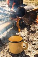 gelbe metalltasse mit heißem kaffee und cezve auf dem hintergrund des lagerfeuers. foto