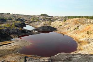 Blick auf einen überfluteten Steinbruch mit rotem Wasser und ausgetrocknete Hügel mit seltener Vegetation. foto