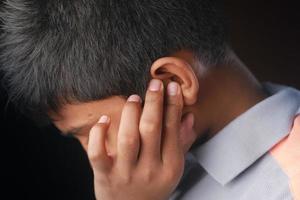 Teenager mit Ohrenschmerzen, die sein schmerzendes Ohr berühren, foto