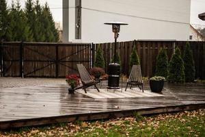 Edelstahl-Metall-Gas-Terrassenheizung im Freien mit Holzstühlen und Topf mit Blumen auf der nassen Terrasse. Ort zum Entspannen. foto