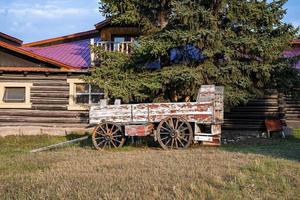 Alter veralteter Wagen unter Baum gegen Blockhaus an sonnigen Tagen foto