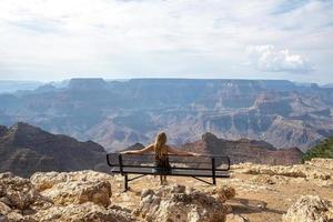 Frau, die den Grand Canyon betrachtet, während sie auf einer Bank sitzt foto