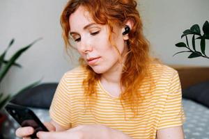 glückliches rothaariges mädchen, das musik hört, zu hause in drahtlosen kopfhörern foto