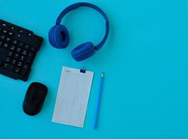 flacher Home-Office-Schreibtisch. Arbeitsbereich mit Laptop, Kopfhörer, Bleistift, Wecker und einem Blatt Papier für Notizen auf blauem Hintergrund. Draufsicht weiblicher Hintergrund. foto