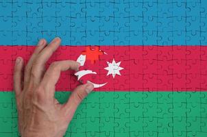 Die aserbaidschanische Flagge ist auf einem Puzzle abgebildet, das die Hand des Mannes zum Falten vervollständigt foto