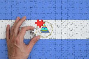 Die Nicaragua-Flagge ist auf einem Puzzle abgebildet, das die Hand des Mannes zum Falten vervollständigt foto