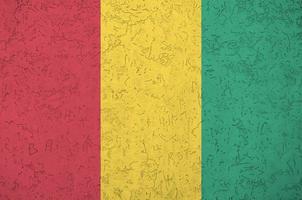 guinea-flagge in hellen farben auf alter reliefputzwand dargestellt. strukturierte Fahne auf rauem Hintergrund foto