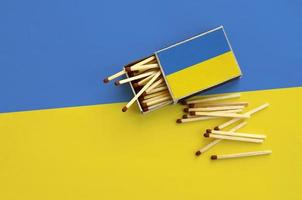 Die ukrainische Flagge ist auf einer offenen Streichholzschachtel abgebildet, aus der mehrere Streichhölzer fallen und auf einer großen Flagge liegt foto