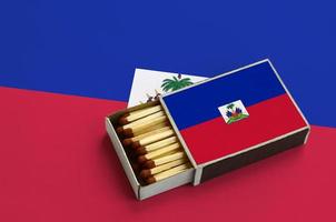 Die Haiti-Flagge wird in einer offenen Streichholzschachtel gezeigt, die mit Streichhölzern gefüllt ist und auf einer großen Flagge liegt foto