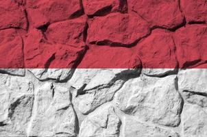 Monaco-Flagge in Lackfarben auf der alten Steinmauer in der Nähe dargestellt. strukturiertes banner auf felswandhintergrund foto