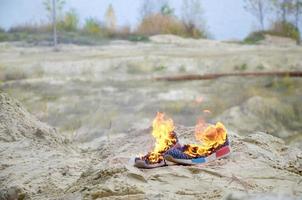 brennende sportschuhe oder turnschuhe in feuer stehen an der sandstrandküste. Sportler ausgebrannt. körperliche anstrengung während des trainingskonzepts foto