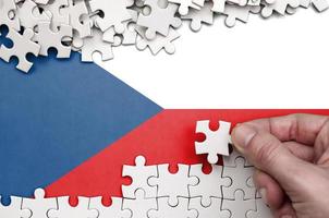 Die tschechische Flagge ist auf einem Tisch abgebildet, auf dem die menschliche Hand ein weißes Puzzle faltet foto