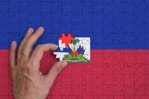Die Haiti-Flagge ist auf einem Puzzle abgebildet, das die Hand des Mannes zum Falten vervollständigt foto