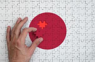 Die japanische Flagge ist auf einem Puzzle abgebildet, das die Hand des Mannes zum Falten vervollständigt foto