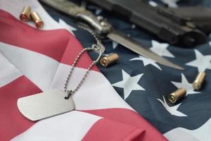 Army Dog Tag Token mit 9-mm-Kugeln und Pistole liegen auf der gefalteten Flagge der Vereinigten Staaten foto