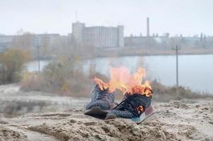 brennende sportschuhe oder turnschuhe in feuer stehen an der sandstrandküste. Sportler ausgebrannt. körperliche anstrengung während des trainingskonzepts foto