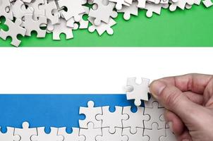 die flagge von sierra leone ist auf einem tisch abgebildet, auf dem die menschliche hand ein weißes puzzle faltet foto