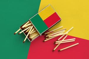 Die Benin-Flagge wird auf einer offenen Streichholzschachtel gezeigt, aus der mehrere Streichhölzer fallen und auf einer großen Flagge liegt foto