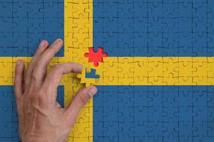 Die schwedische Flagge ist auf einem Puzzle abgebildet, das die Hand des Mannes zum Falten vervollständigt foto