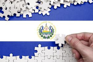 die flagge von el salvador ist auf einem tisch abgebildet, auf dem die menschliche hand ein weißes puzzle faltet foto