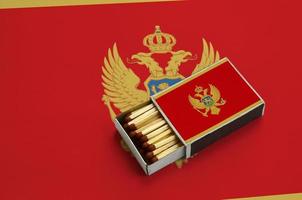 Die montenegro-Flagge wird in einer offenen Streichholzschachtel gezeigt, die mit Streichhölzern gefüllt ist und auf einer großen Flagge liegt foto
